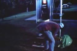 A man picking up stuff from the ground by a payphone