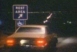 A car driving up to a rest area atop a hill late at night