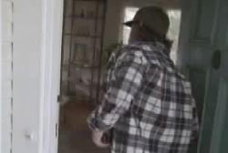 A man in a flannel shirt and hat walking into the Santos home