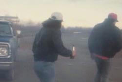Two young men next to a truck holding beer in a field