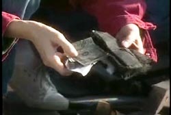 A kneeling person taking cash out of Lauria's purse