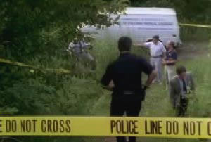 Police investigators entering a section of the woods that are walled off by yellow crime tape