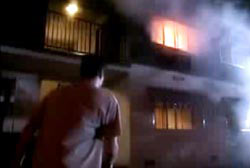 A man looking up at a second story apartment thats engulfed in flames
