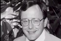 Smiling Michael Franke wearing a suit and tie and glasses 