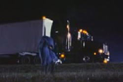 Man carrying a covered body into a field away from his semi-truck