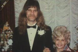 Terri with arm around son Tim McClure with a long mullet, mustache, and wearing a tuxedo