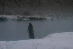 A woman in a black dress walking off a snowy bank into freezing water