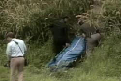 Police investigators carrying a body in a body bag out of the woods