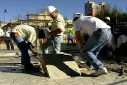 Construction workers lifting a small quare out of the ground at the Alamo