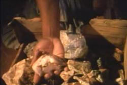 A hand grabing a piece of gold ore out of a wooden container