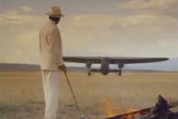 Leon Trabuco with a cane in a white suit and hat standing next to a campfire as a plane lands in the background