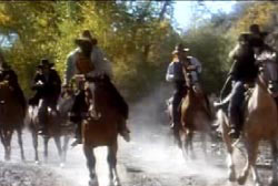A gang of men with cowboy hats and bandanas around their faces riding horses 