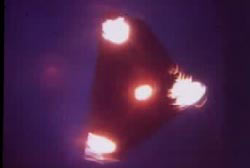 A triangular UFO with light emanating from its corners appears to be spinning in the sky