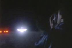 A man holding a home video camera at a larg beam of light in the night sky