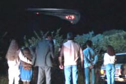 A large group of onlookers staring at a UFO in the night sky