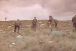 Military presonel holding bags, picking up the debris scattered in the desert