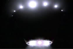 A dark object in the sky with lights around it in a circular pattern (a UFO)