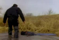 A police investigator wading through mud to reach the remains of their victims