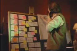 Dan writing on a chalk board filled with post it notes while he talks on a landline phone 