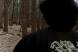 A man with curly black hair walking through the woods