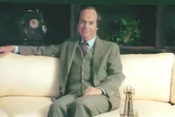 Ed Baker sitting on a white couch in a suit and tie