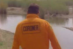 A coroner in an orange jumper walking up to a swampy body of water