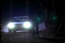 A car with its headlights pointing towards a silhouetted man