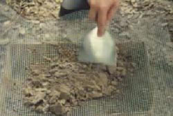 Person holding a small shoverl sifting through dirt on metal mesh sheet