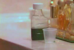 A bottle of medicine on a bathroom countertop thats filled with green liquid