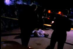 Police investigators surrounding the dead body of Ted in the middle of a street with yellow tape around the scene