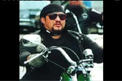 Randy Yager with goatee, wearing a bandanna glasses and riding a chopper motorcycle