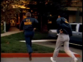 U.S. Marshals drawing their pistols while running towards a house
